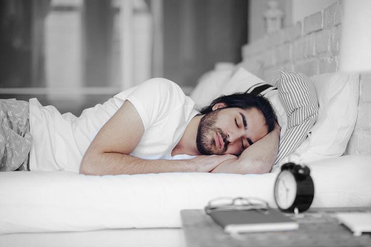 A man asleep on his side, with an alarm clock by the bed