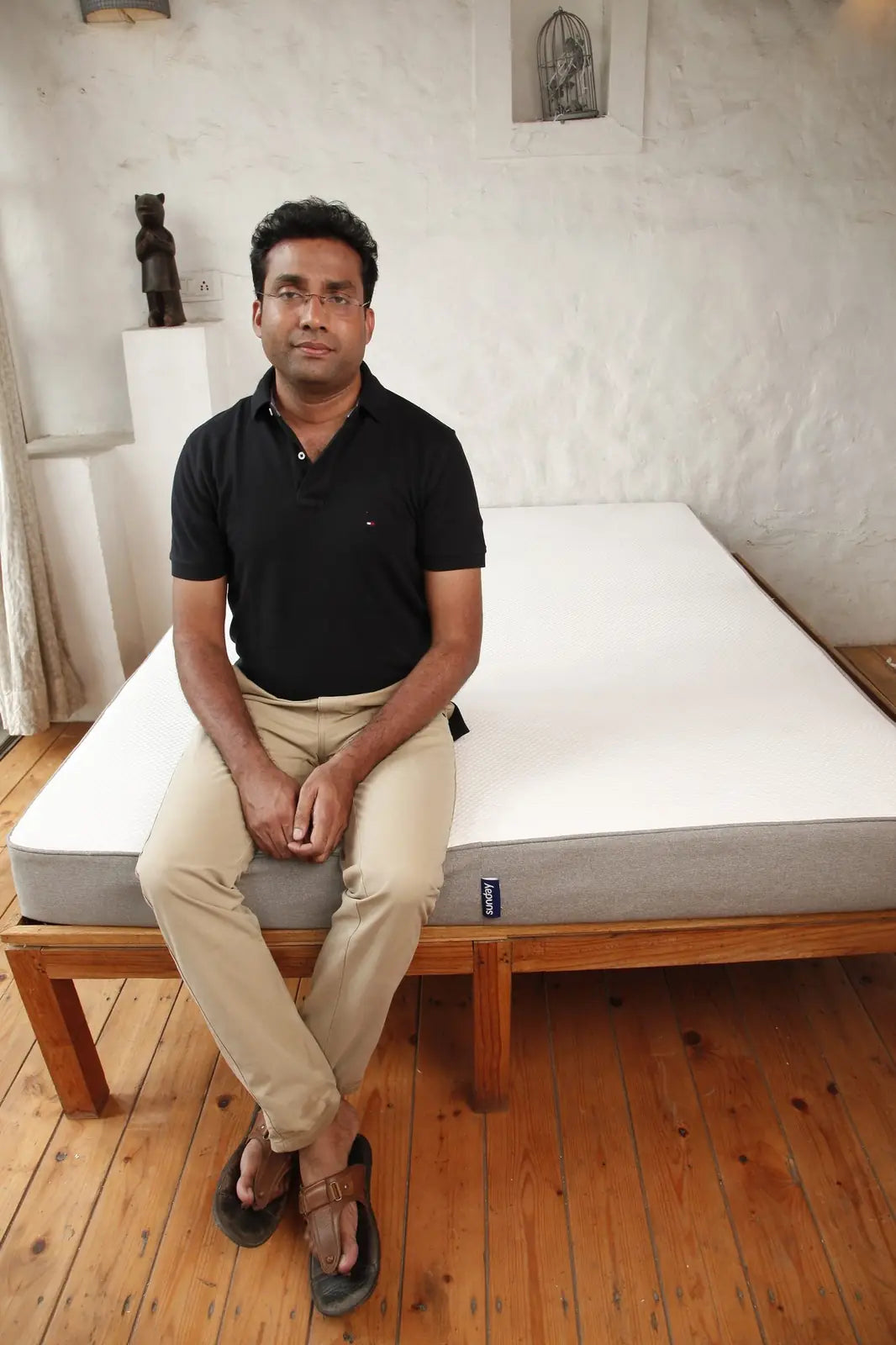A man sitting on the edge of a Sunday mattress on a wooden bed frame